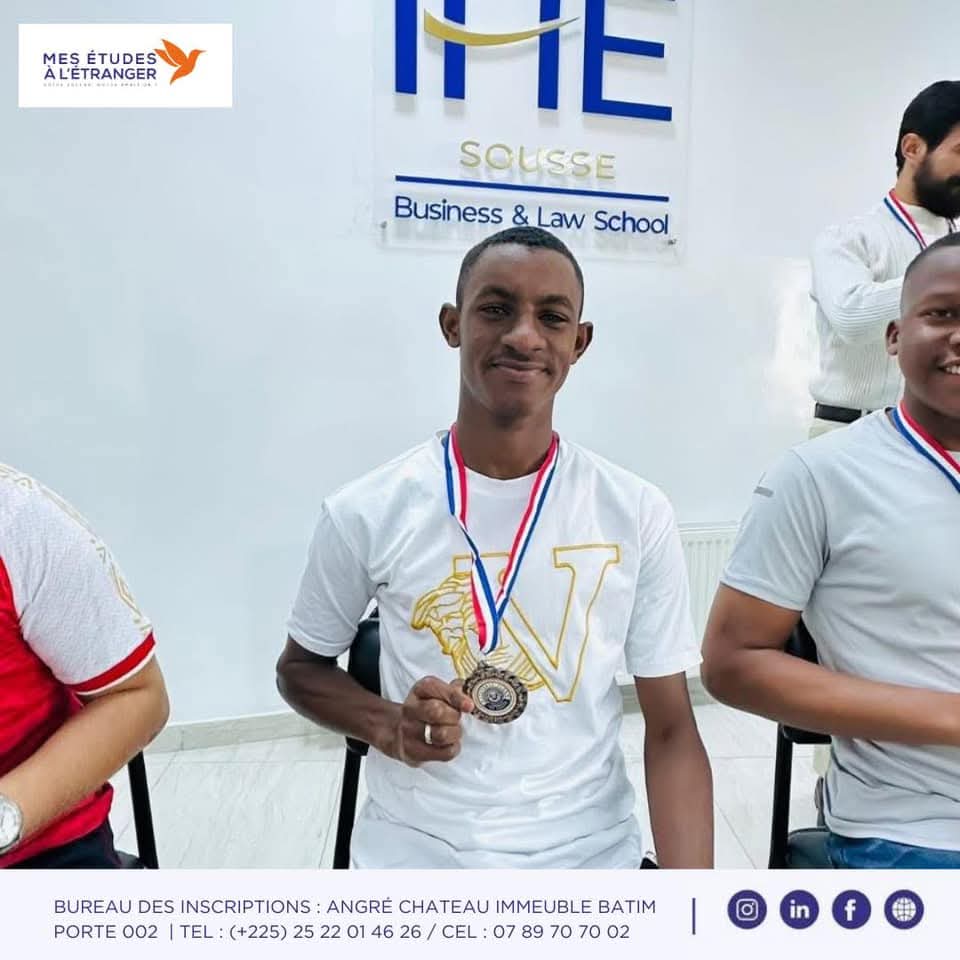 Étudiant souriant présentant sa médaille devant le logo IHE Sousse